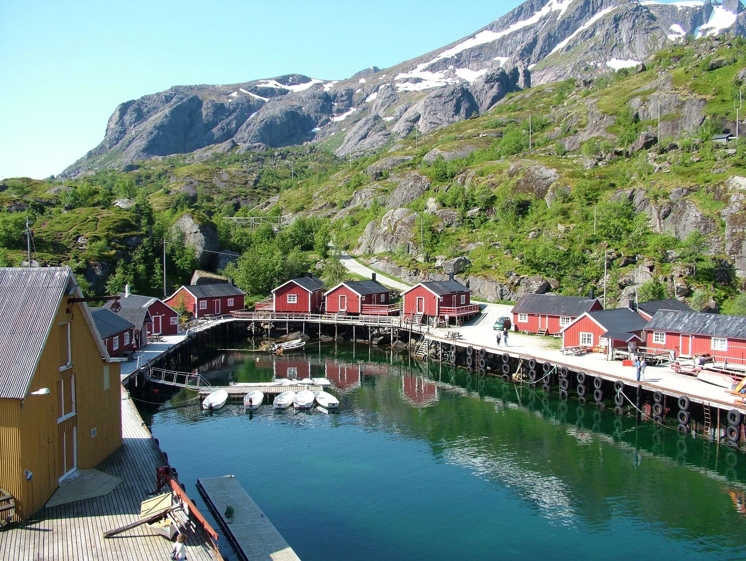 Harbor with red buildings and a yellow house, surrounded by mountains.