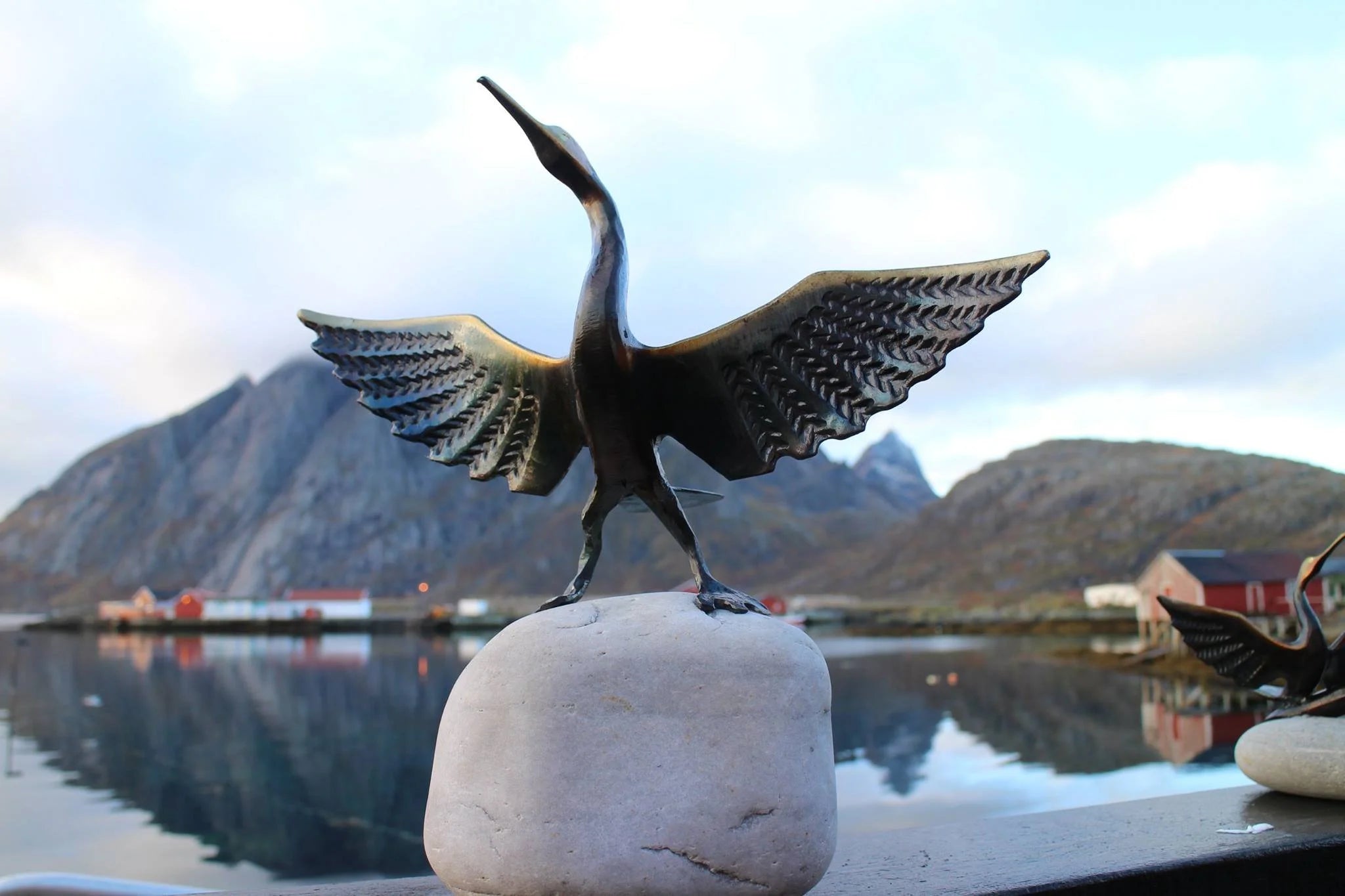 Bronze sculpture of a bird on a rock with a mountainous landscape in the background