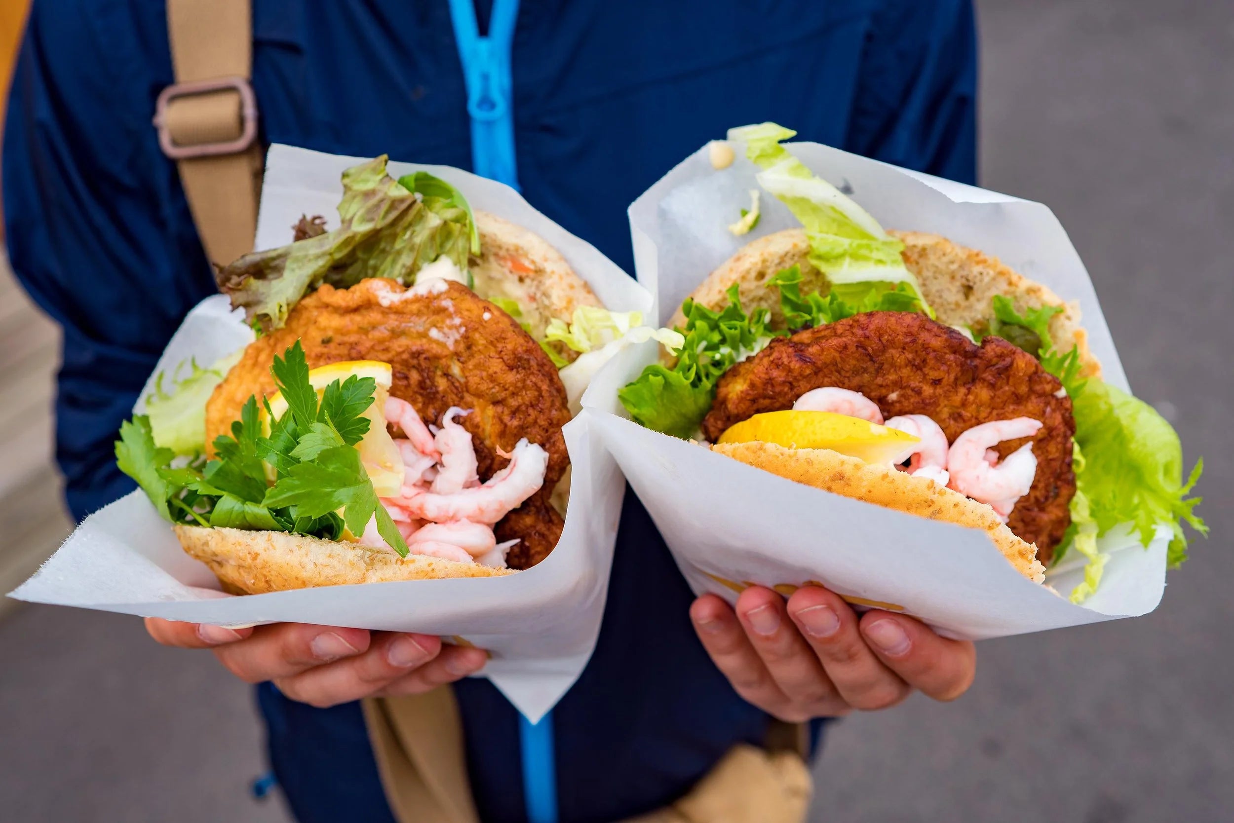 Two hands holding burgers with visible ingredients on a blurred background