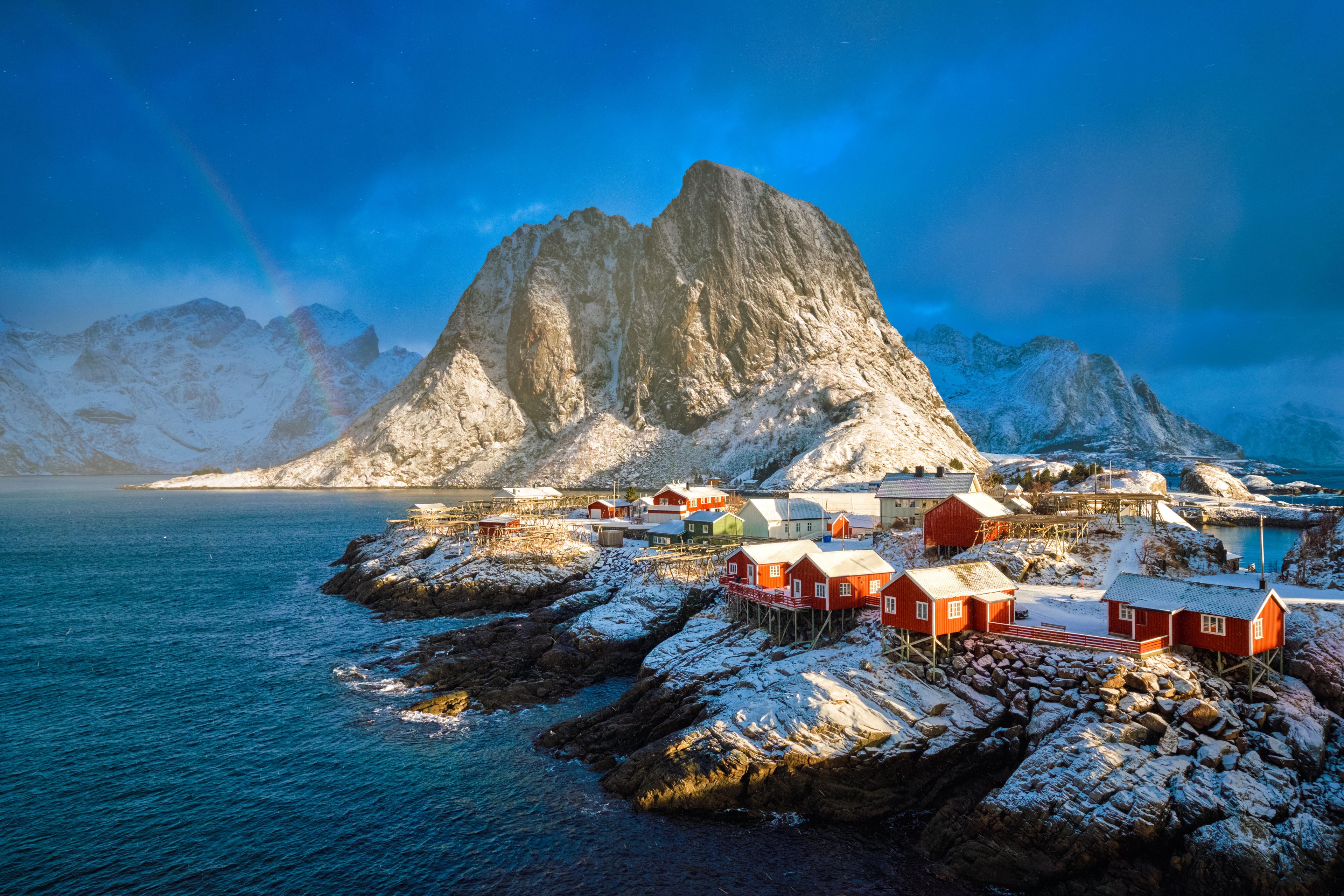 Red cabins on a rocky island with snow-capped mountains and blue sky.
