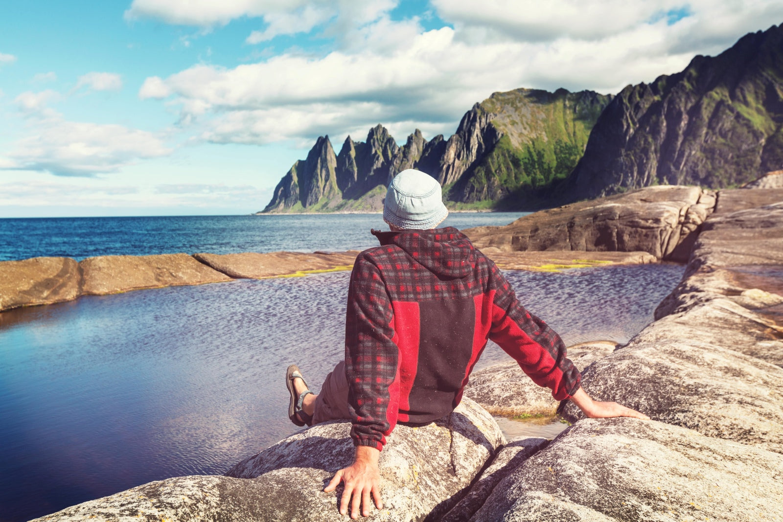 Person sitting on a rock by a scenic coastal landscape with mountains.