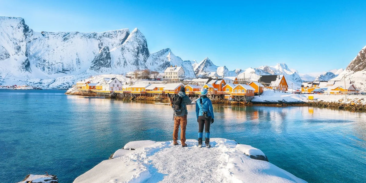 Two people standing on a snow-covered ledge overlooking a冻湖和雪景村庄