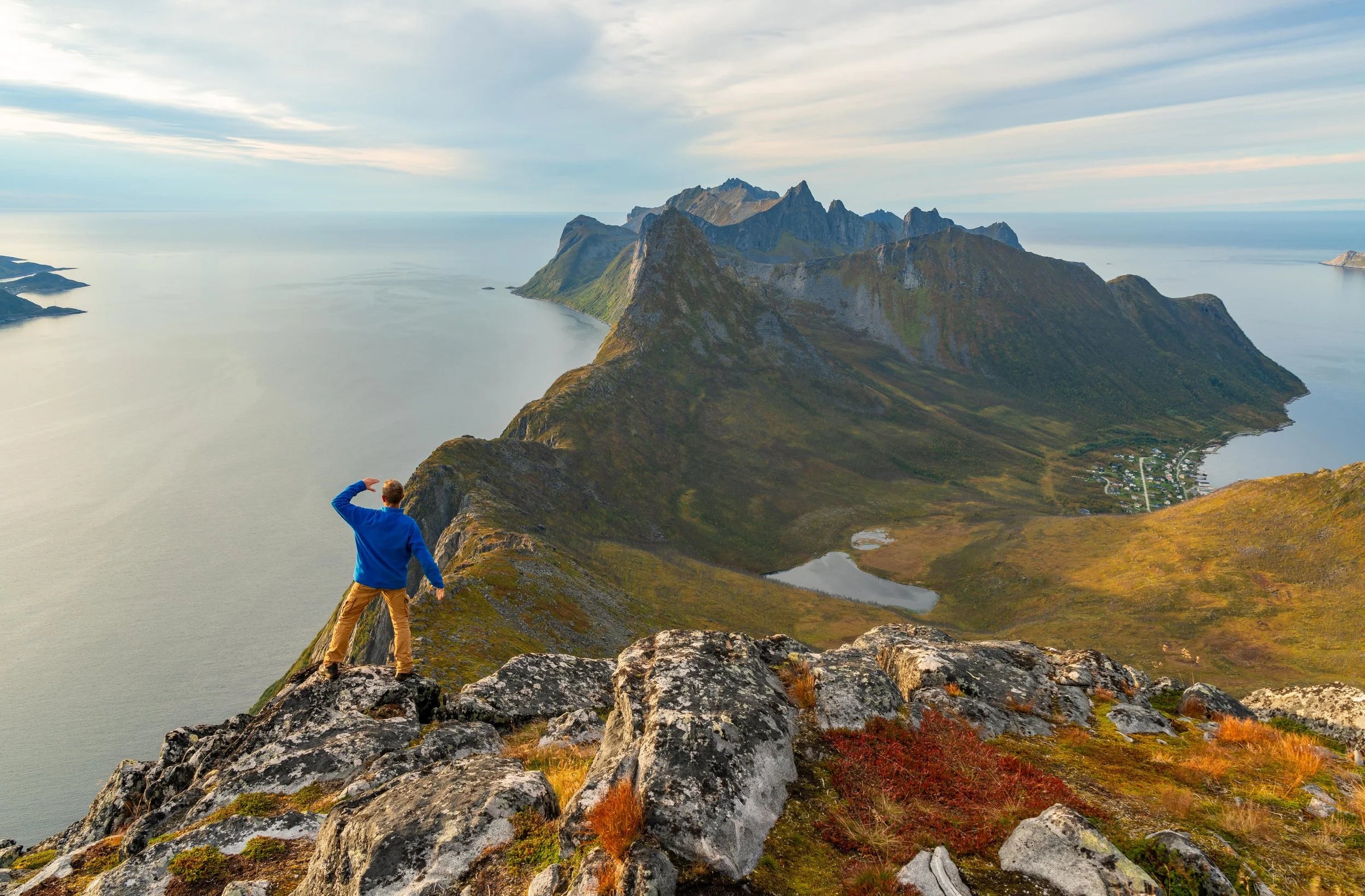 Person standing on a rocky outcrop overlooking a scenic landscape with mountains and water.