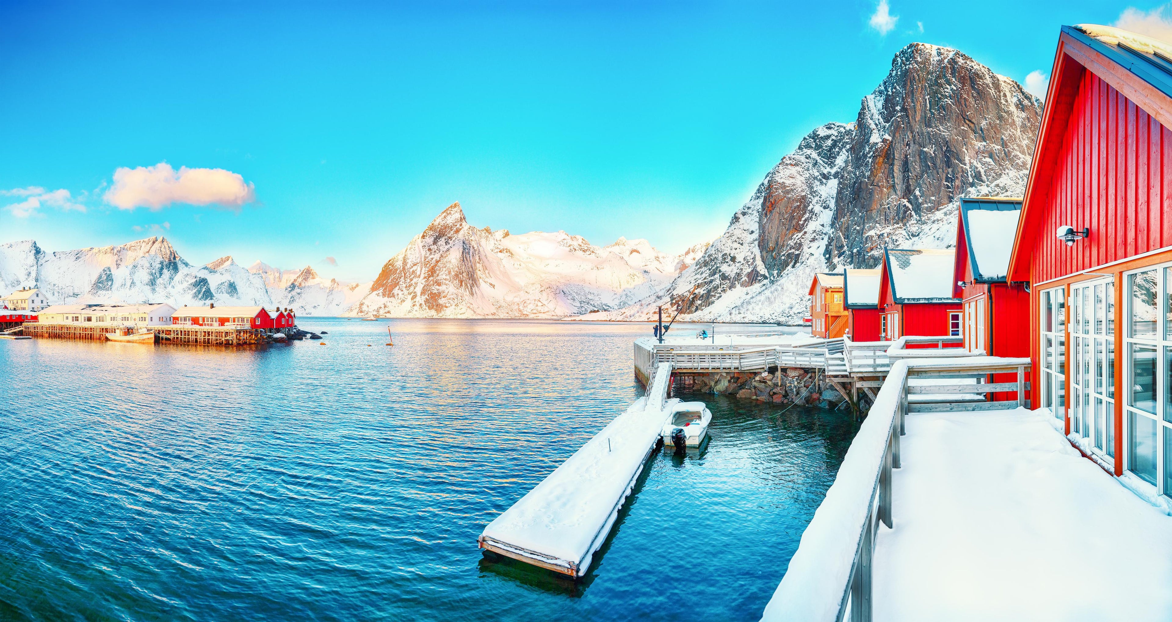 Scenic view of a snowy landscape with red buildings, dock, and mountains.