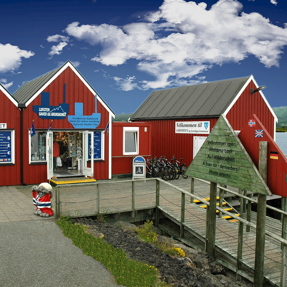 Red wooden buildings with a sign and bicycles on a wooden platform under a blue sky.