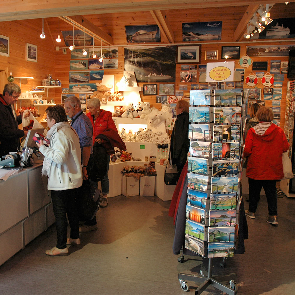 People shopping in a store with a display of postcards and souvenirs.