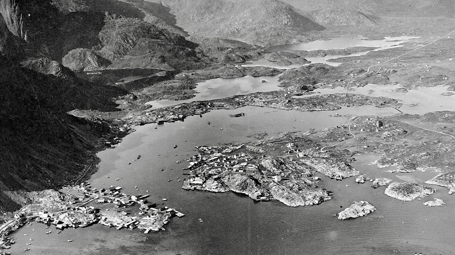 Black and white aerial view of a river landscape with rocky banks and distant mountains.
