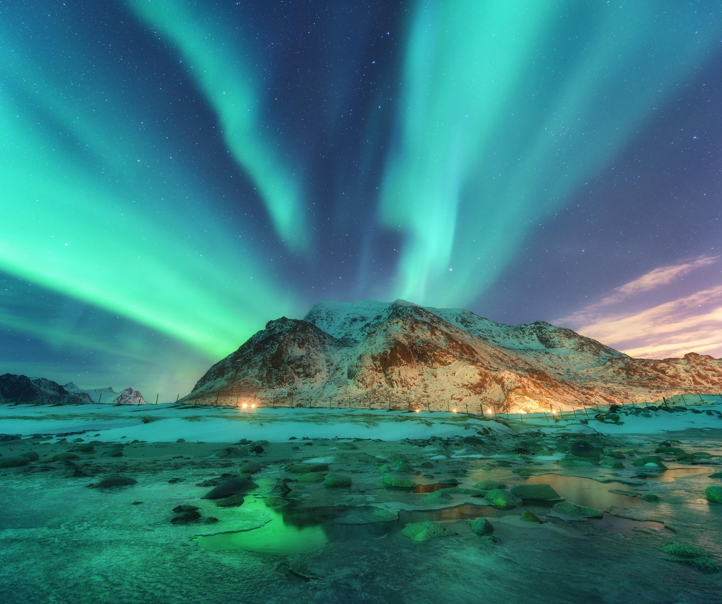 Aurora borealis over a mountainous landscape with snow and rocks.