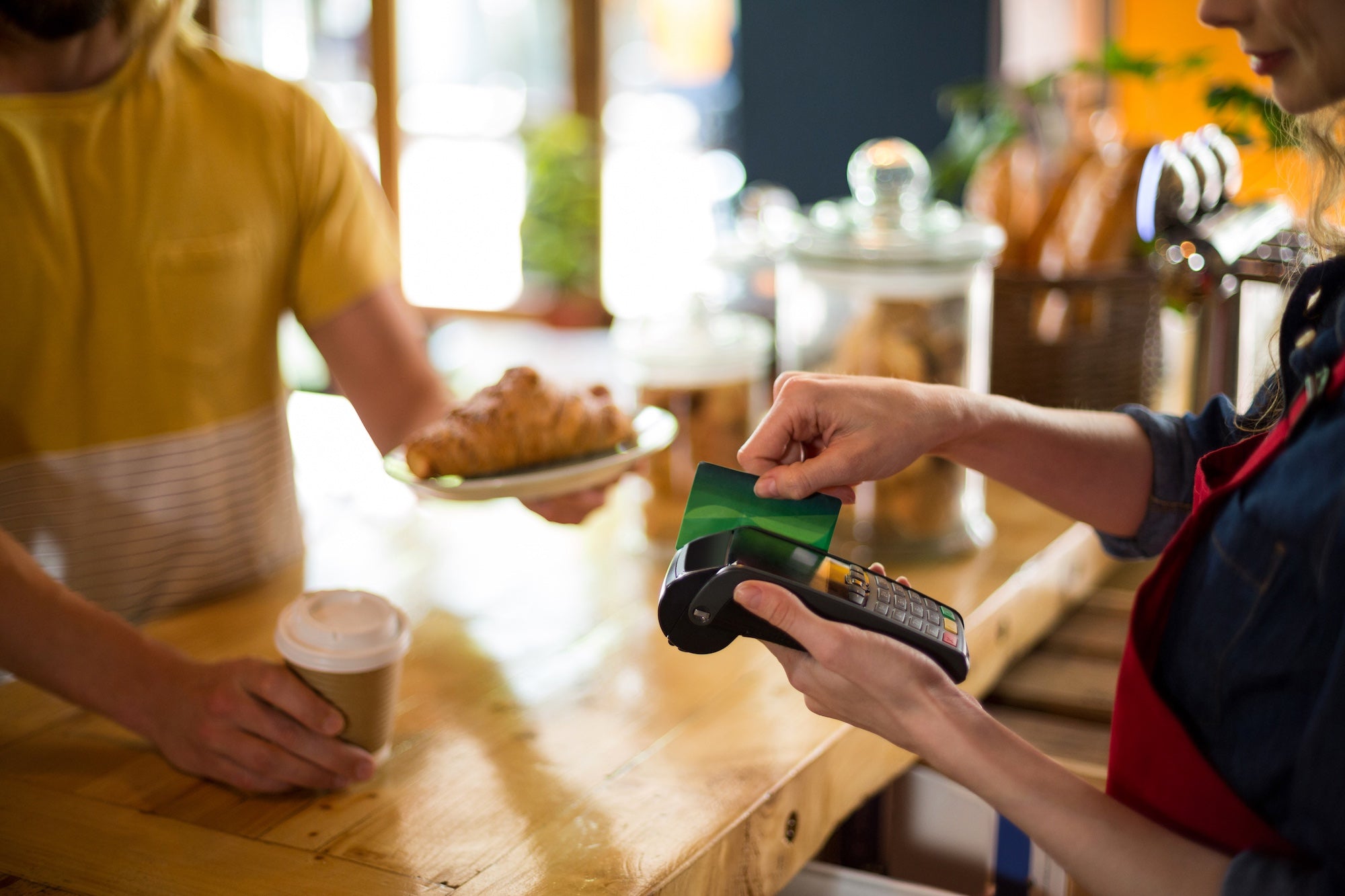 Person paying for a coffee using a contactless payment card at a cafe.
