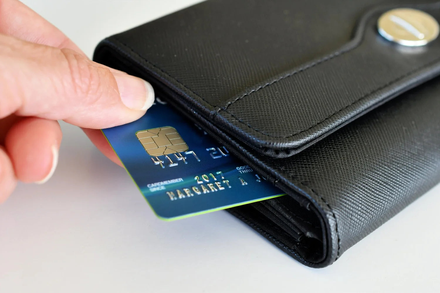 Hand placing a credit card into a black wallet on a light background