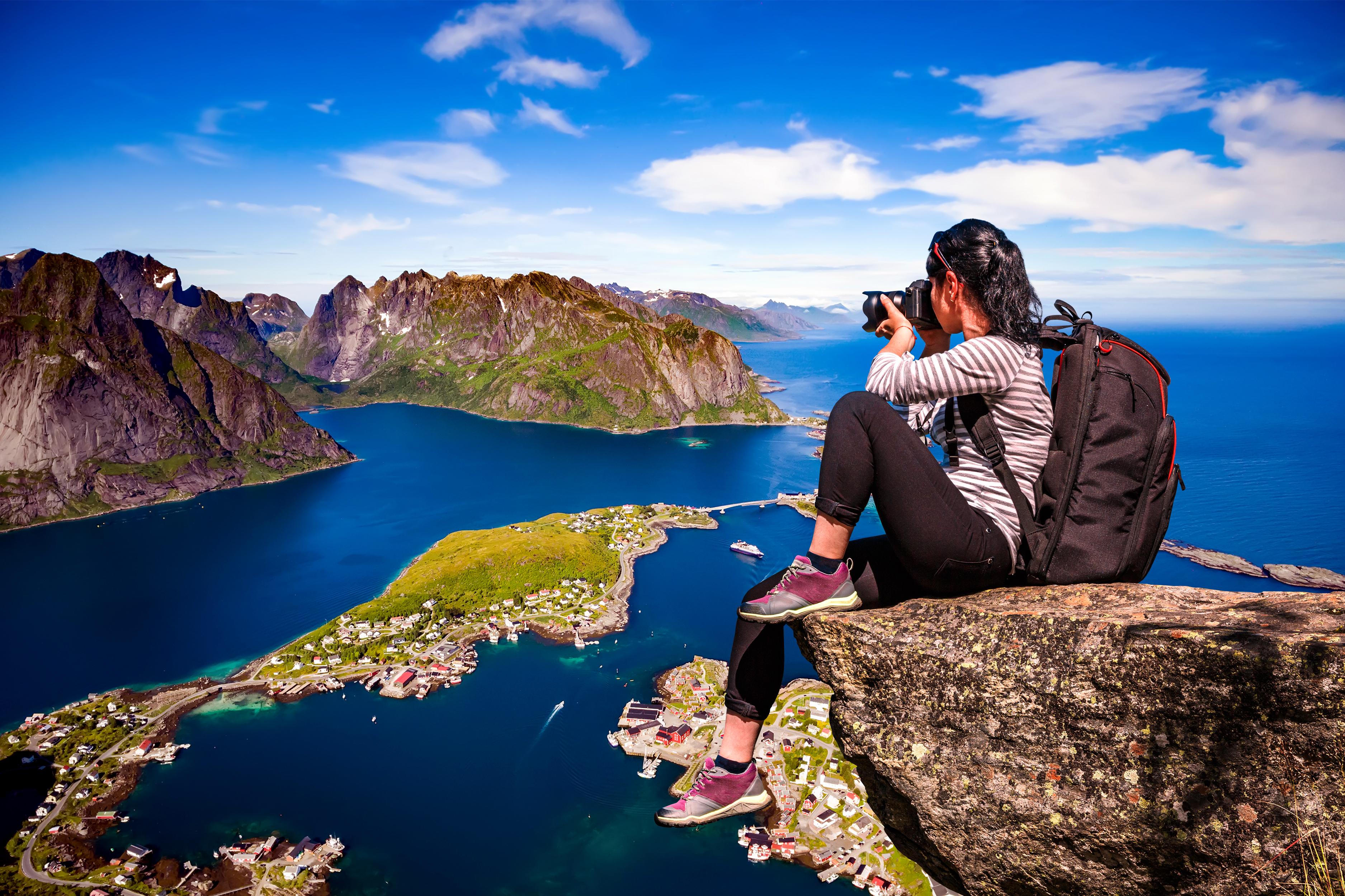 Person taking a photo of a scenic view with mountains and a lake.