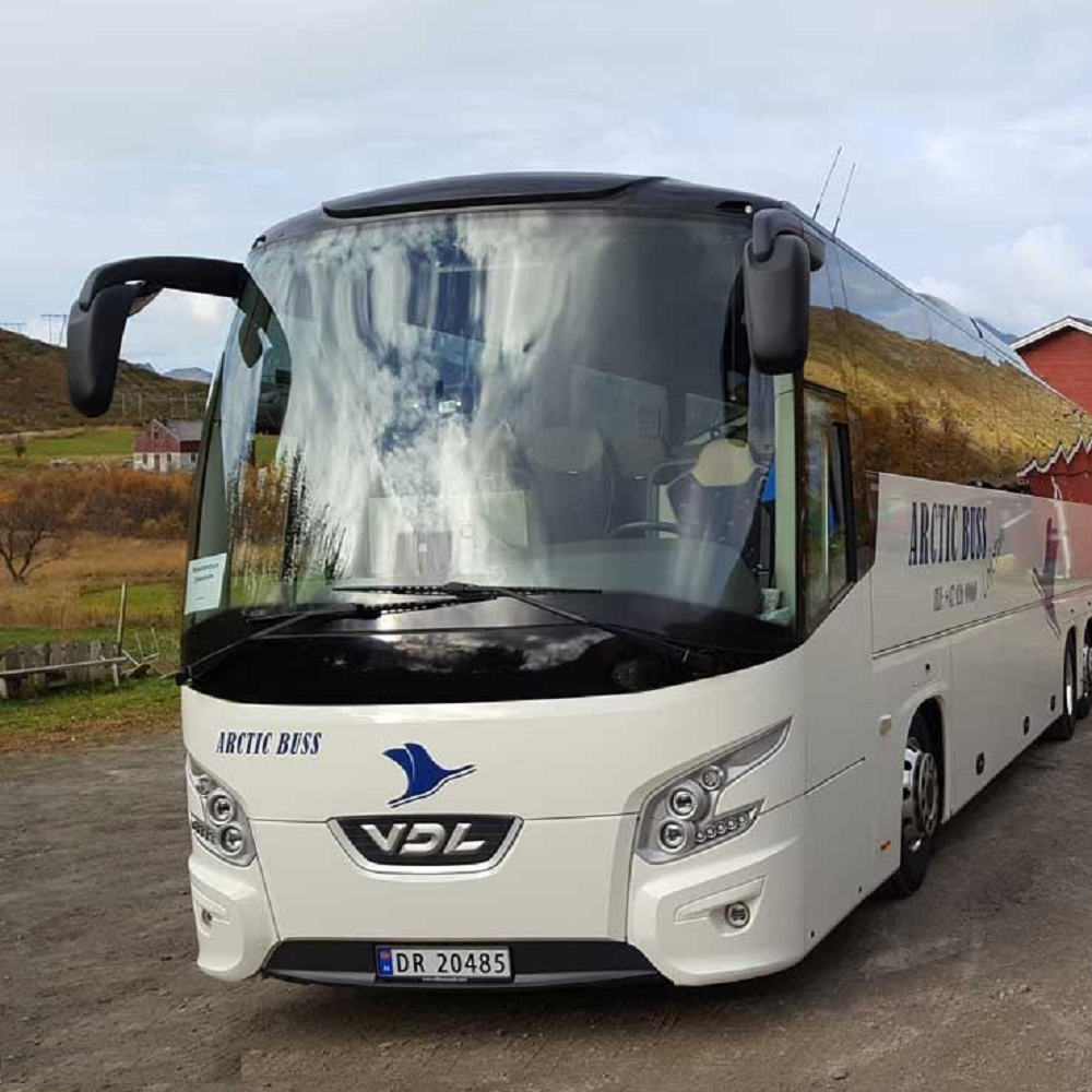 White bus with visible branding on a road with a scenic background